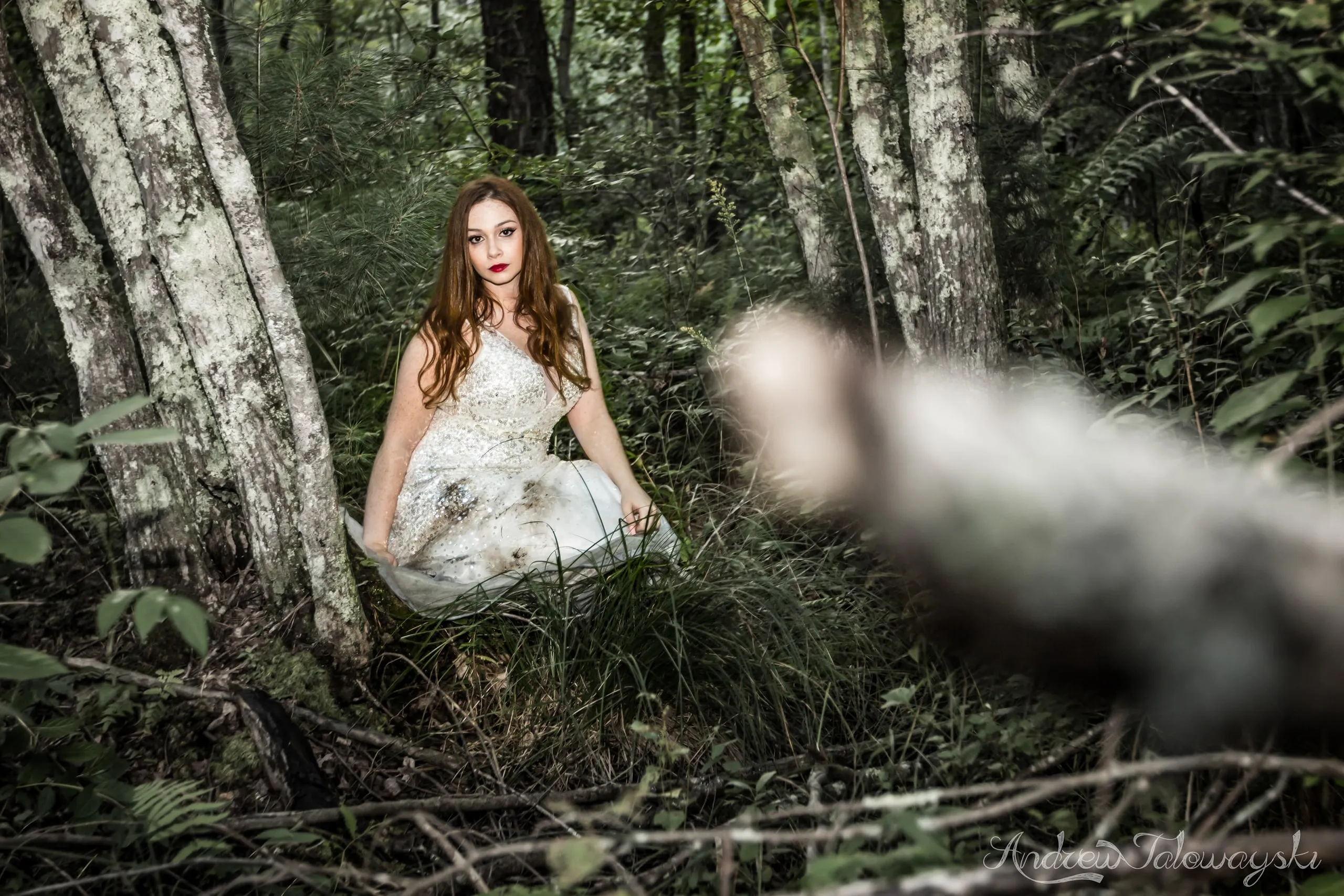 Woman in a white gown sitting among birch trees in a green forest
