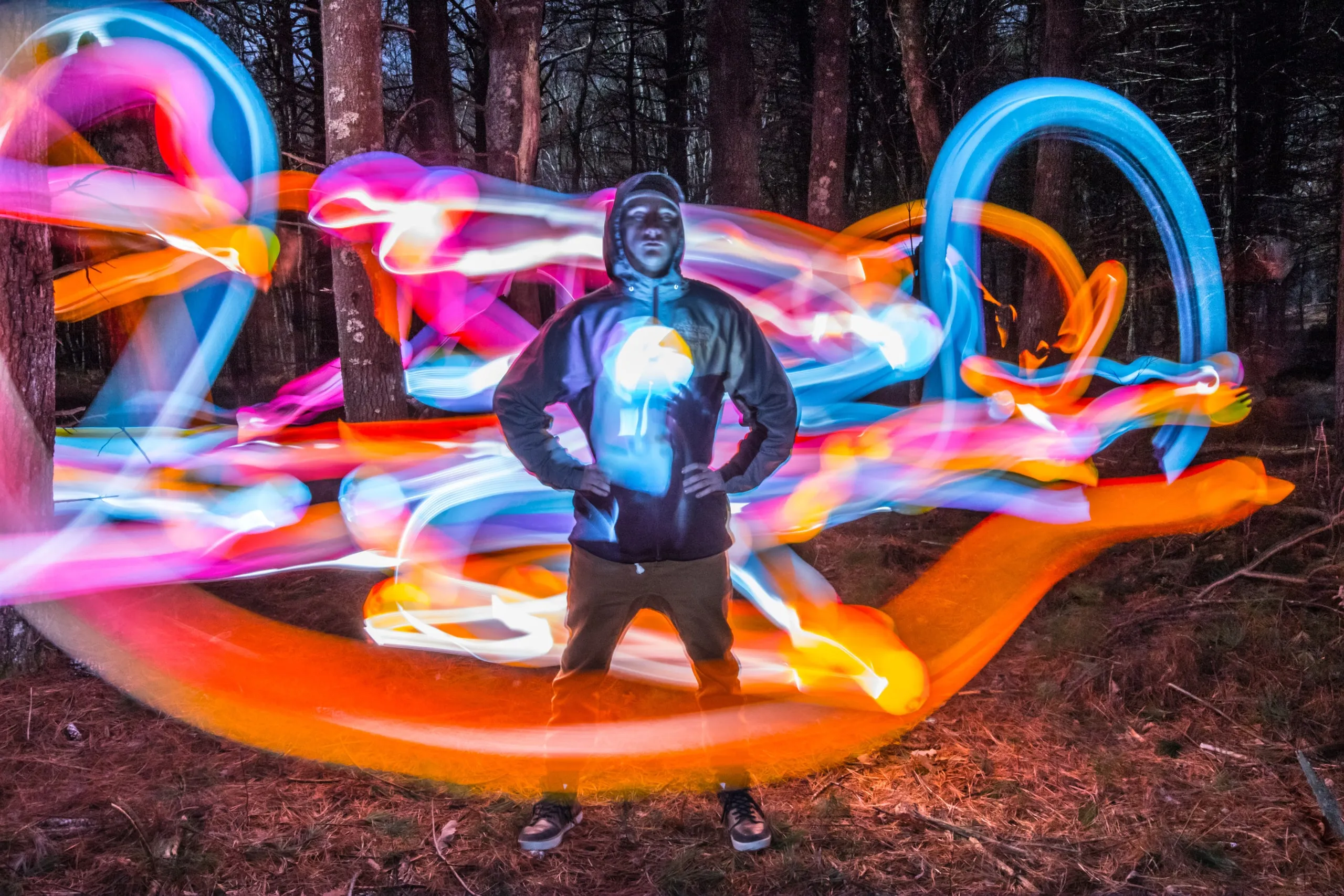 Person outlined by colorful light-painting loops in a dark forest