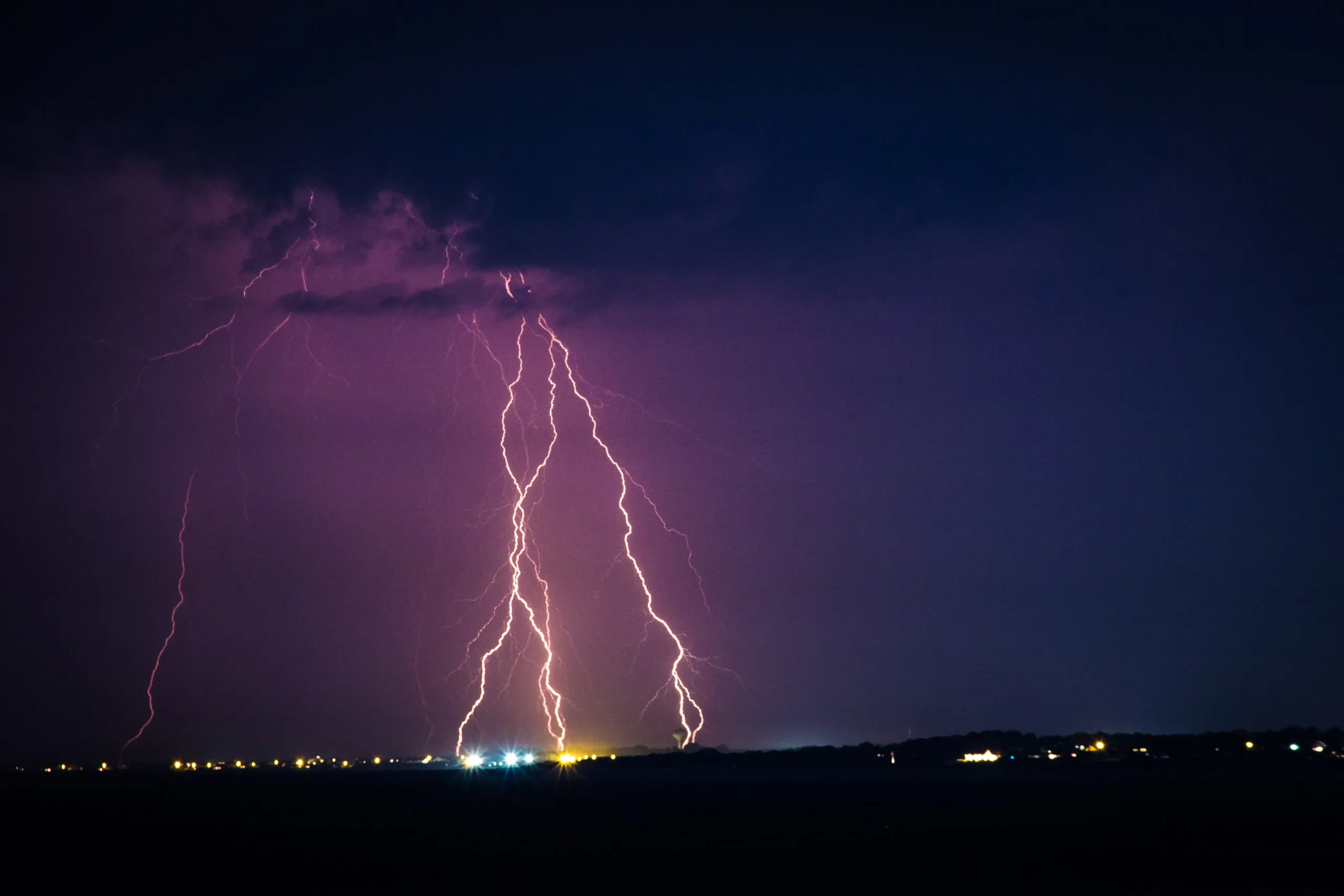 Purple lightning bolts striking over a dark horizon