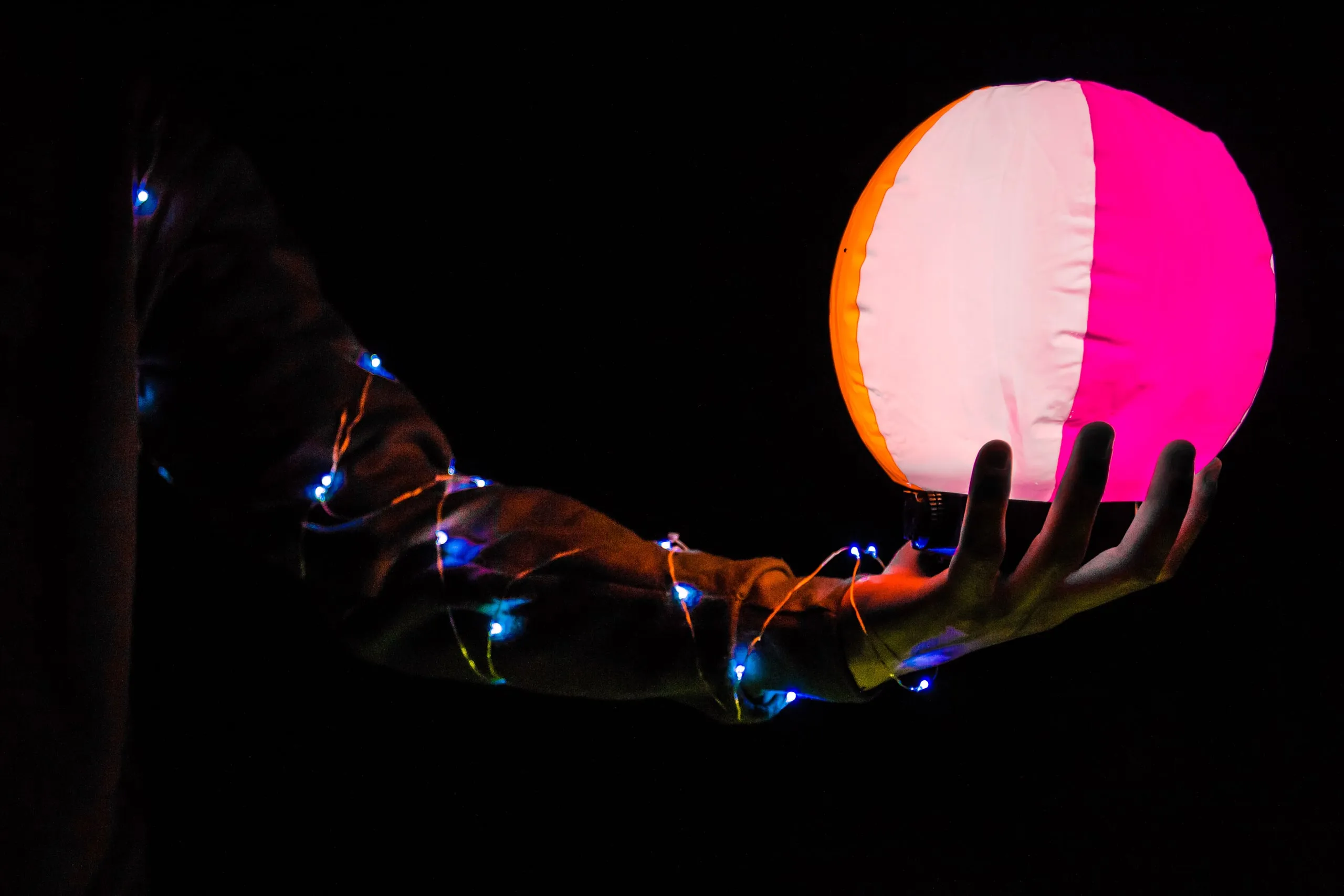 Hand holding a glowing pink and white sphere in the dark