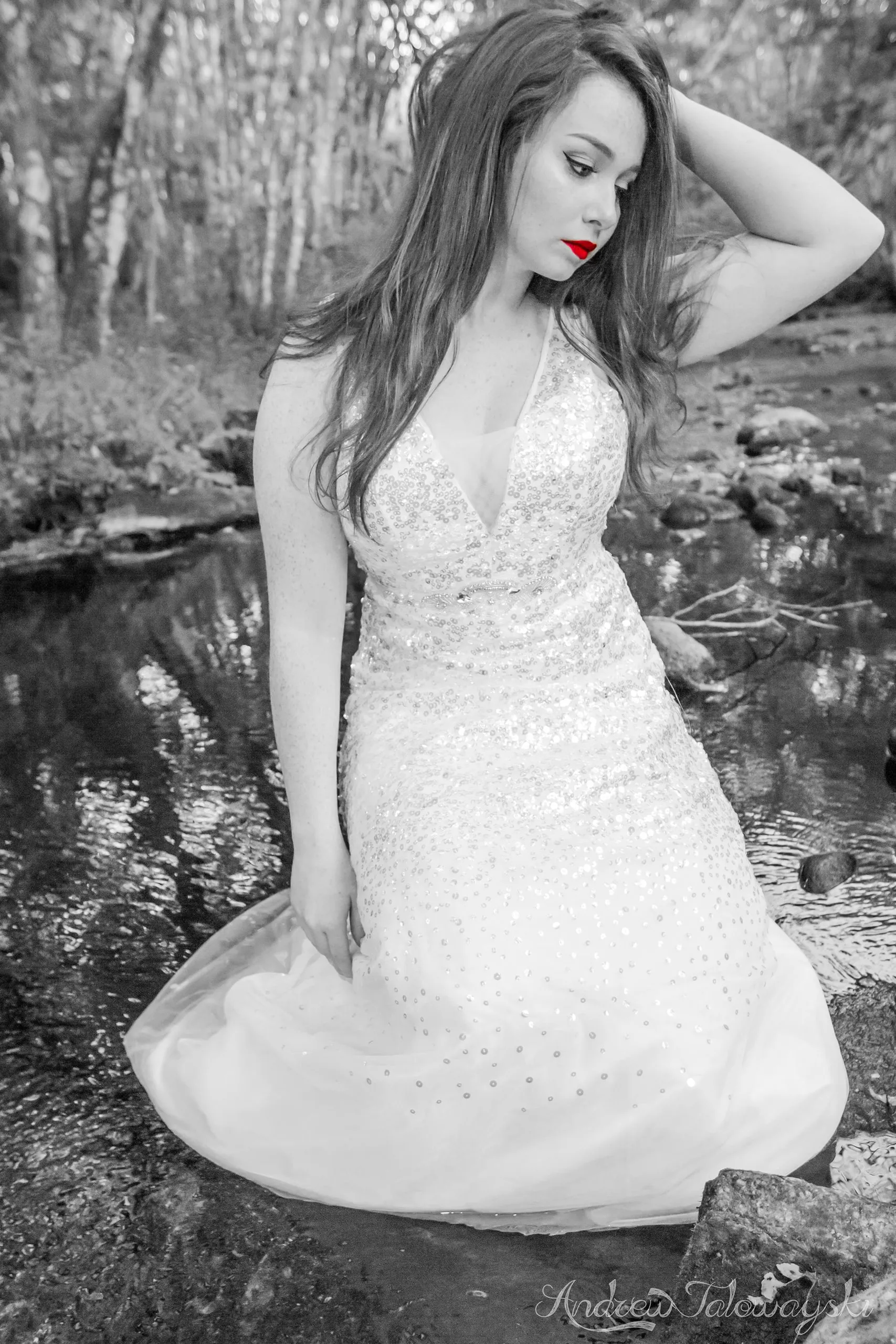 Black-and-white portrait of a woman in a white gown kneeling in the forest
