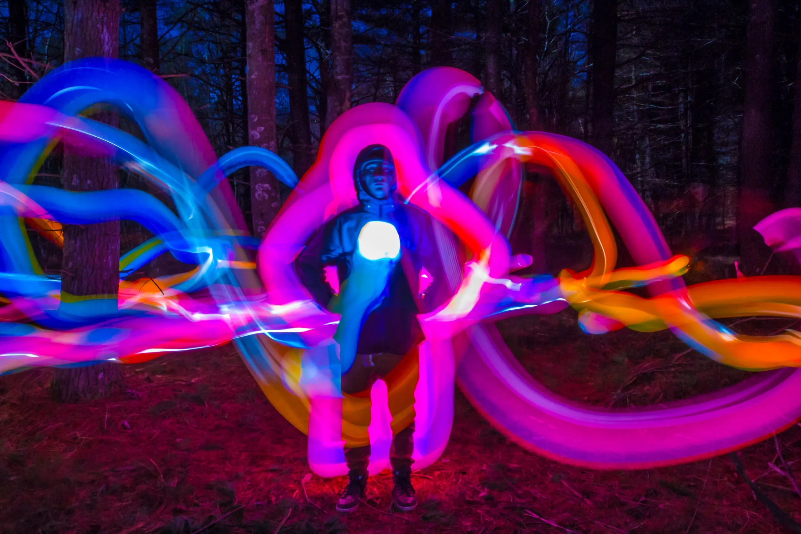 Person wrapped in pink and blue light-painting loops at night