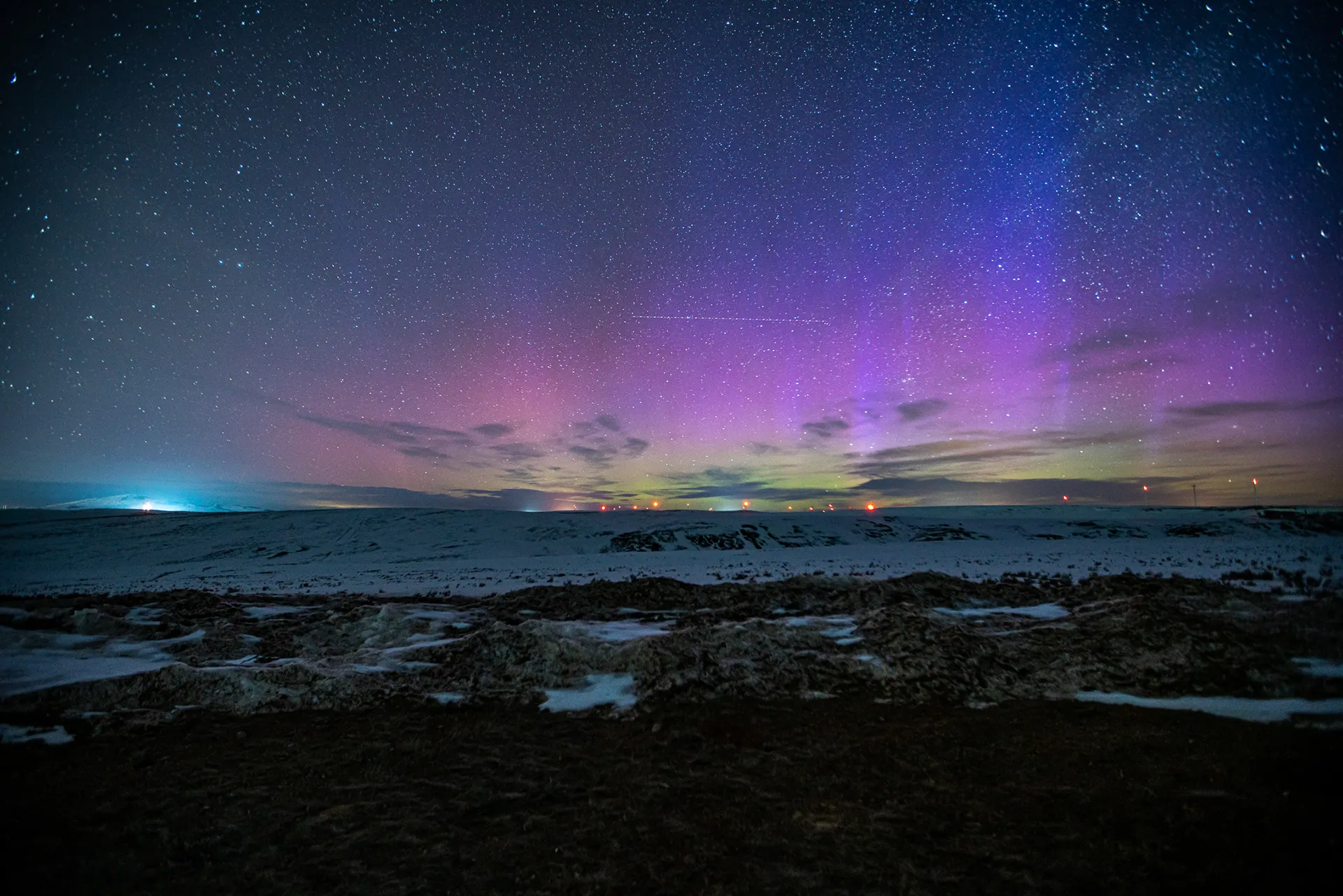 Purple and green aurora borealis over a dark landscape