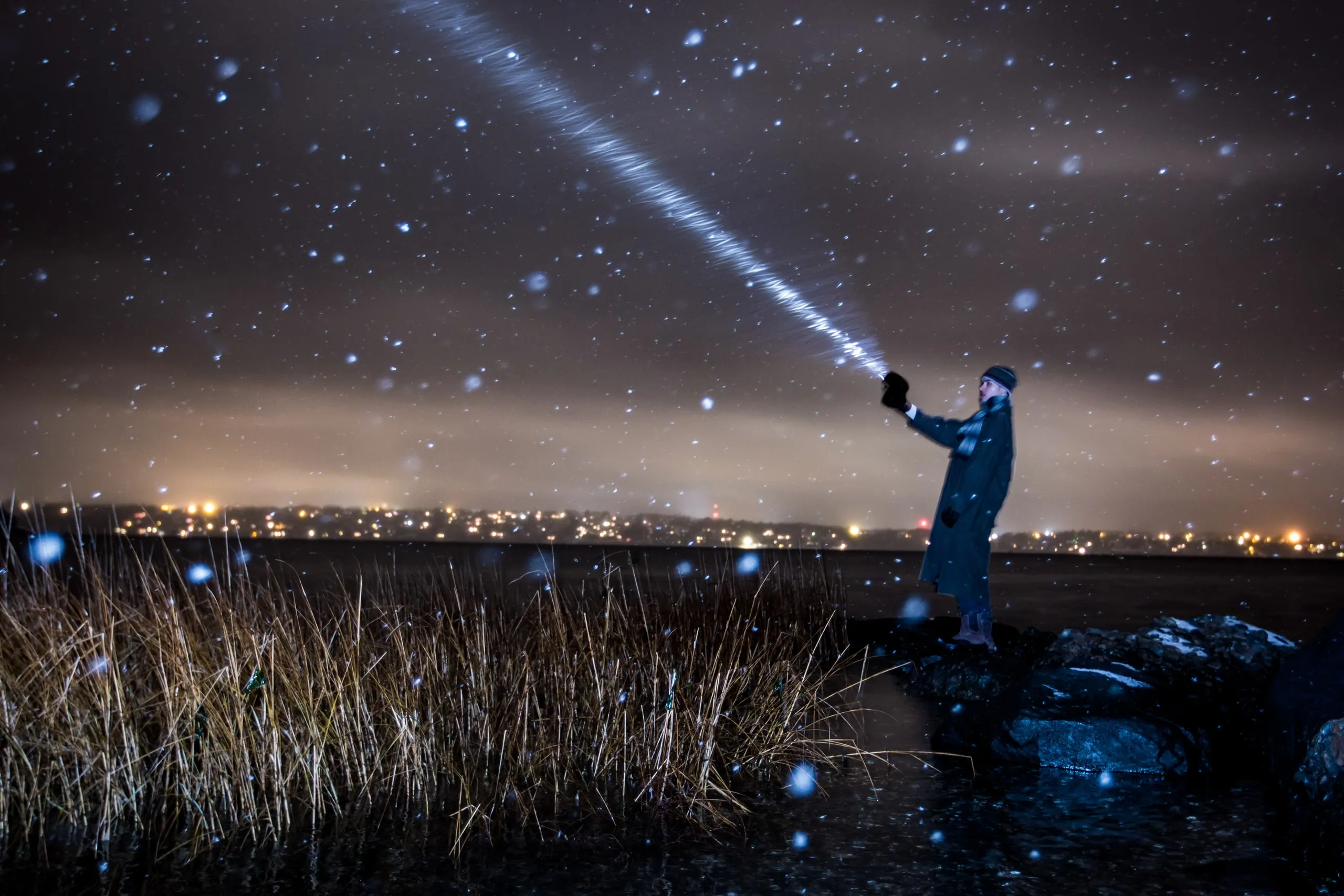 Person shining a flashlight beam into a starry sky over a marsh