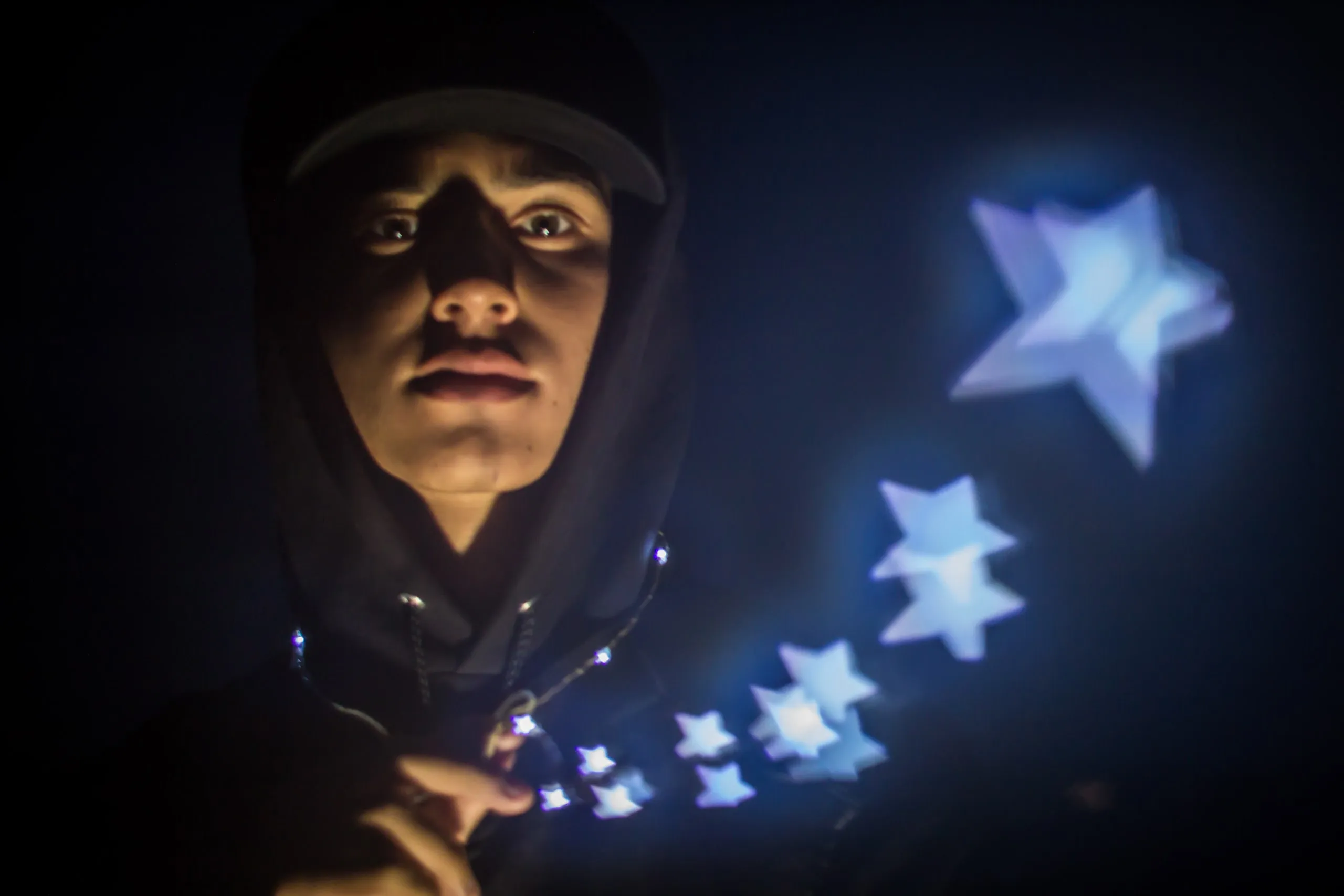 Person in a hood with glowing light-painted stars beside them
