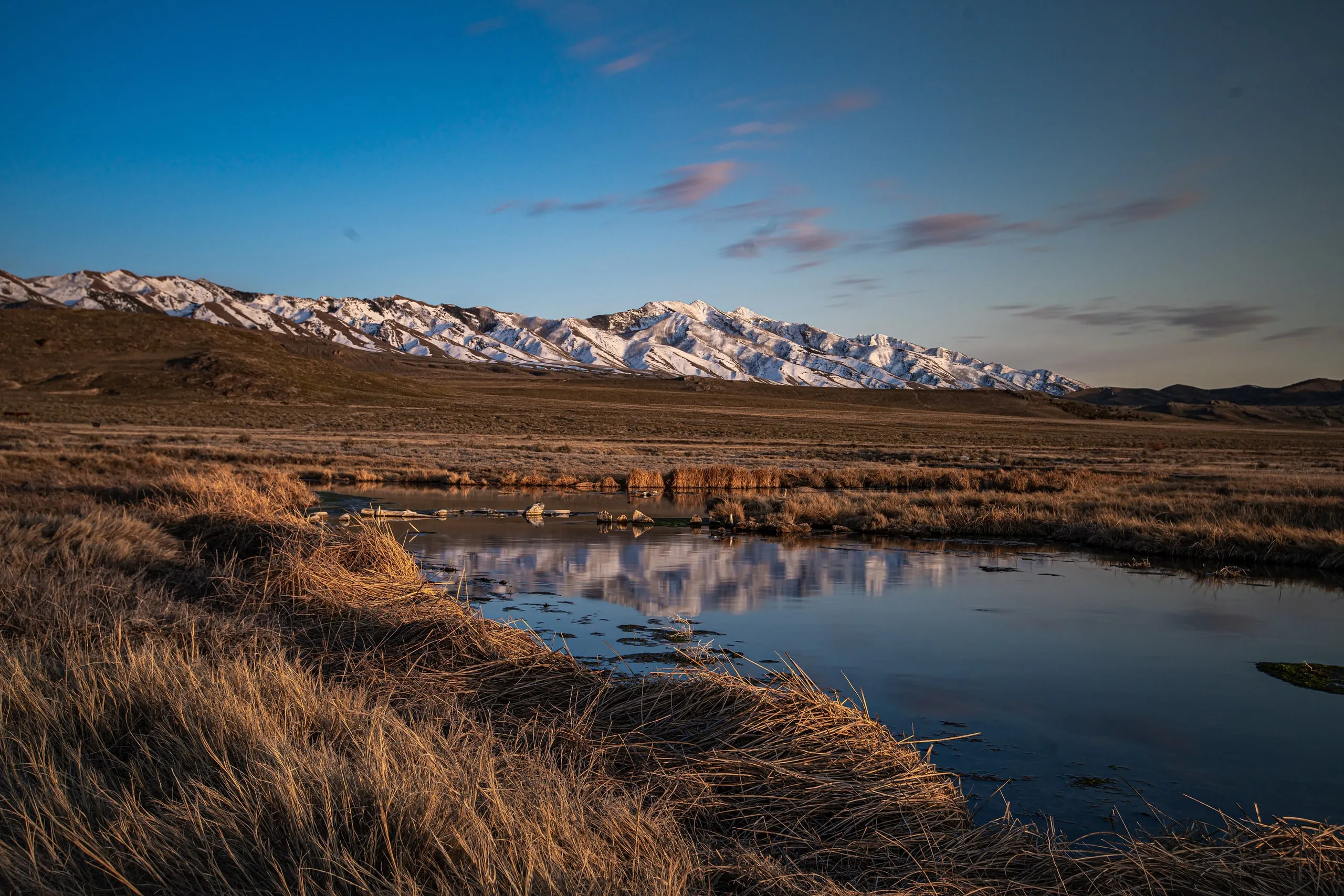 Snow-capped mountains above a marsh pond in Skull Valley at dusk