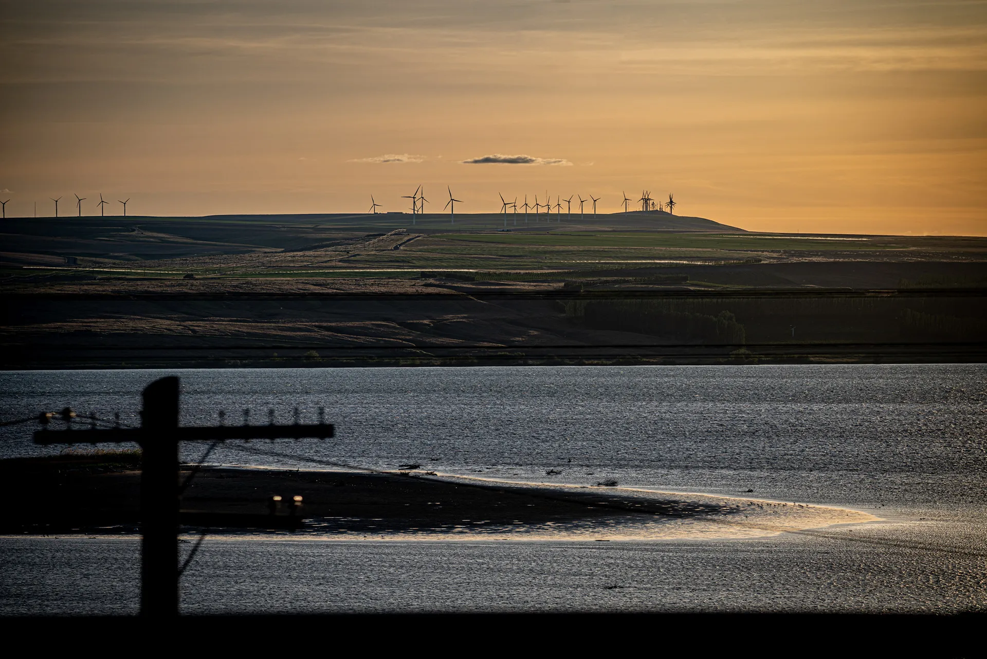 Row of wind turbines on a ridge above a river at sunset