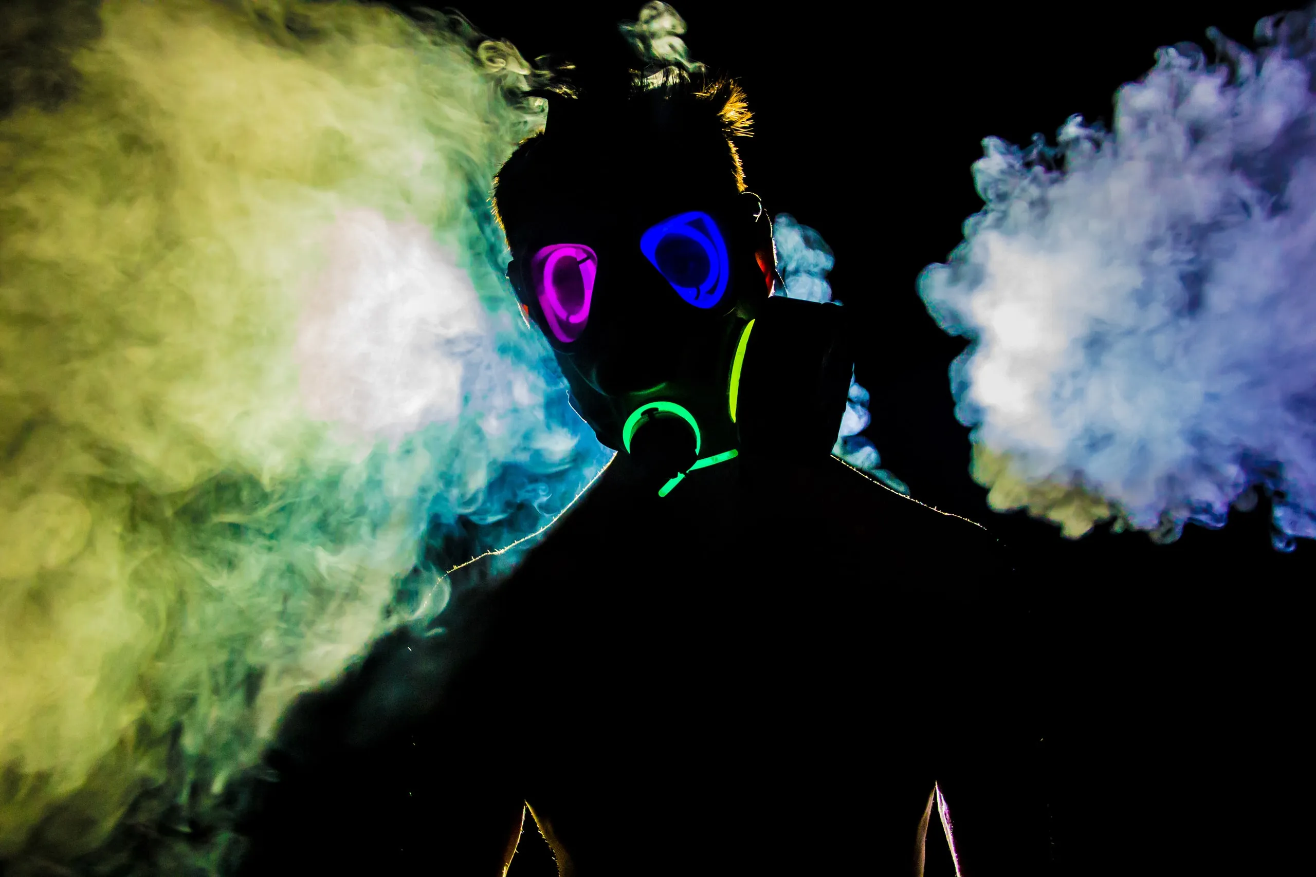 Person in a glowing neon mask exhaling colored smoke