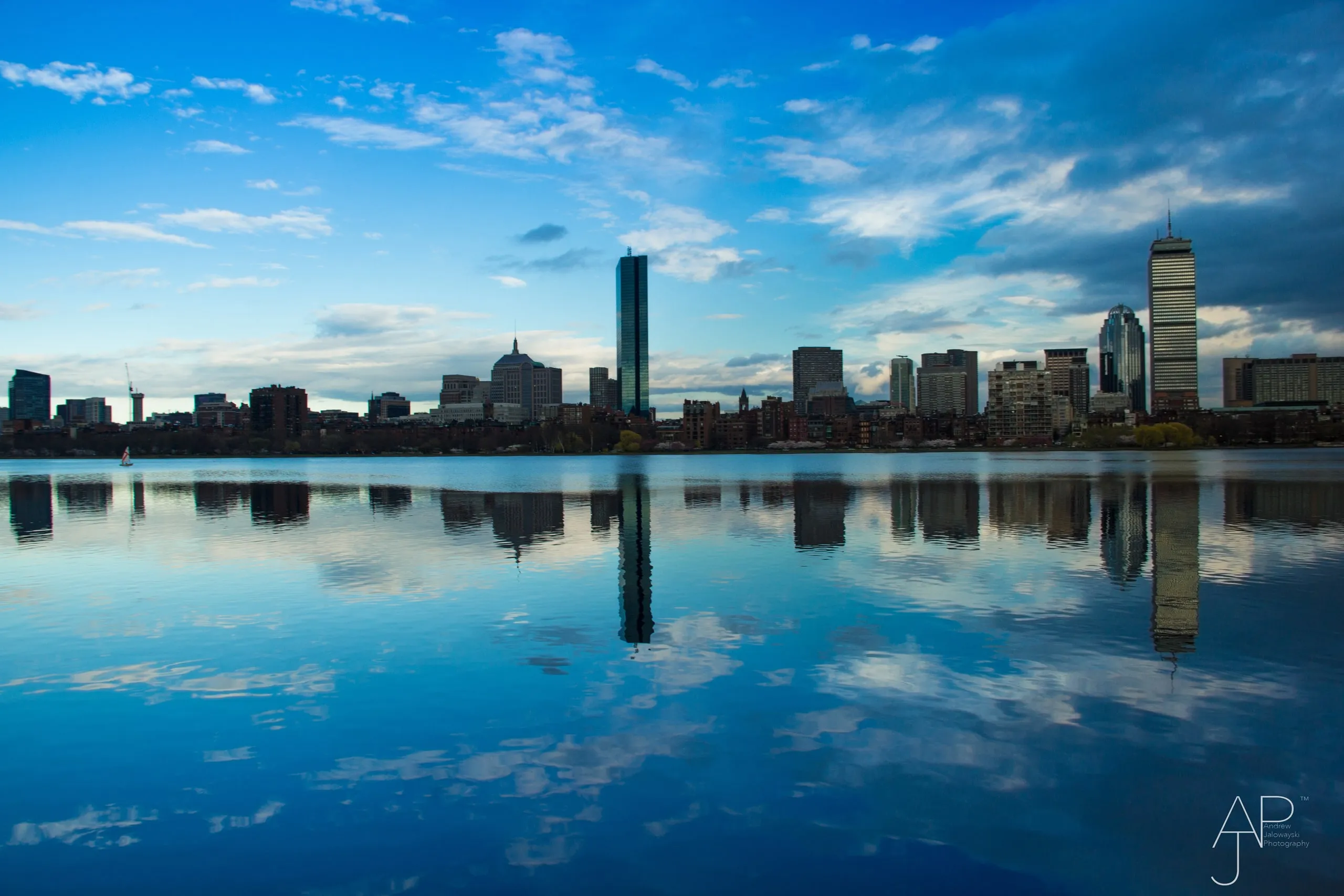 City skyline reflected in still blue water under clouds