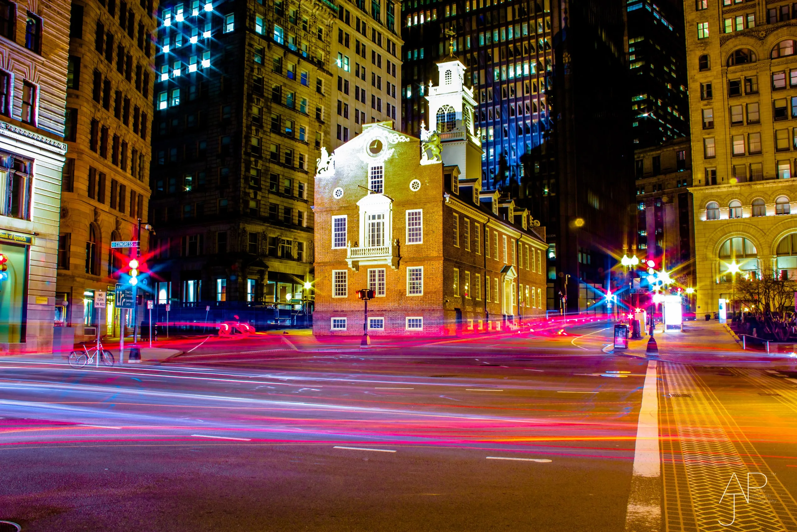 Historic brick building between skyscrapers with light trails from traffic at night